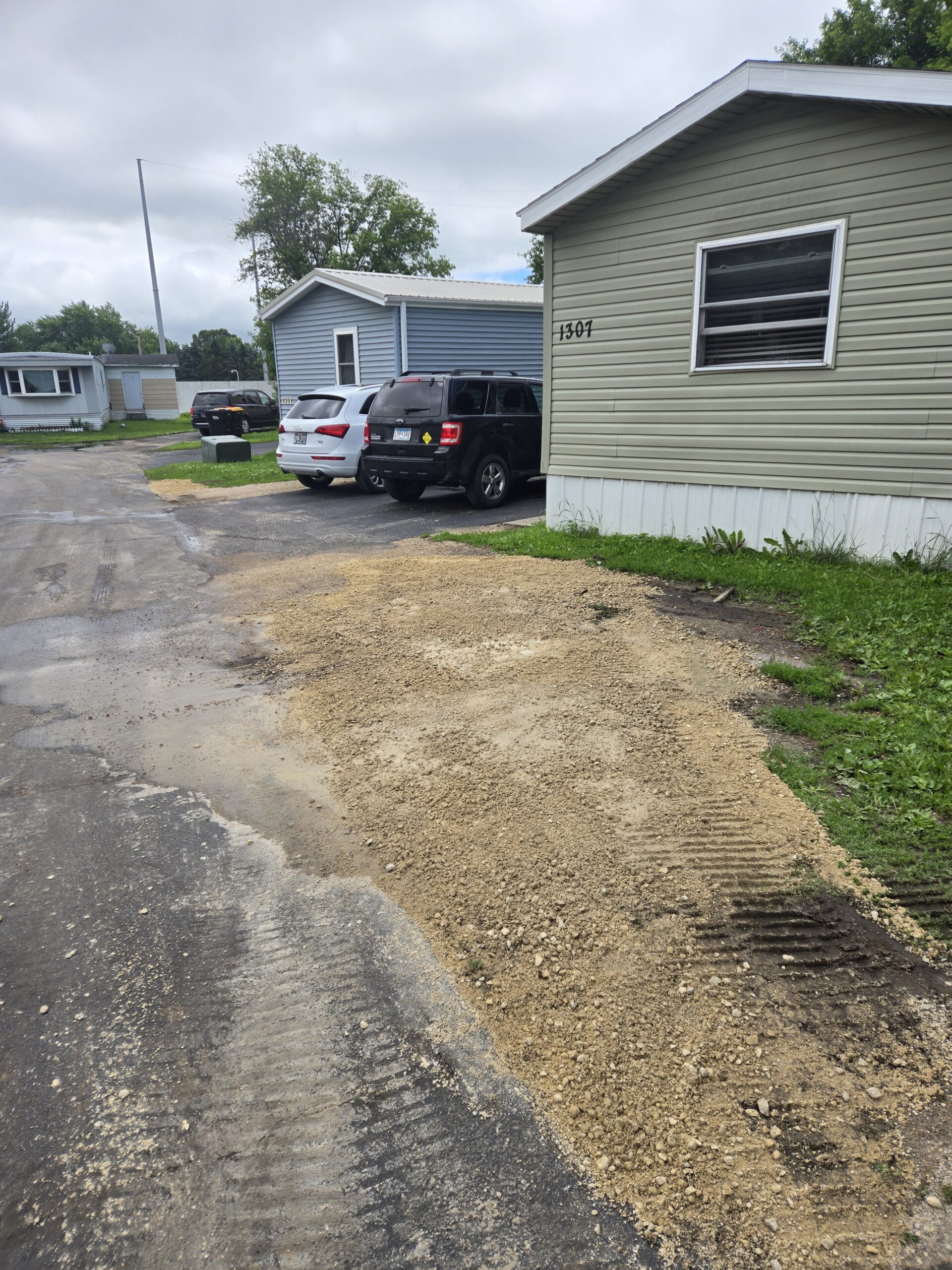 A mobile home with blue shutters and a small trampoline in the yard. A newly laid walkway of light and dark grey pavers leads from the yard to the front steps.