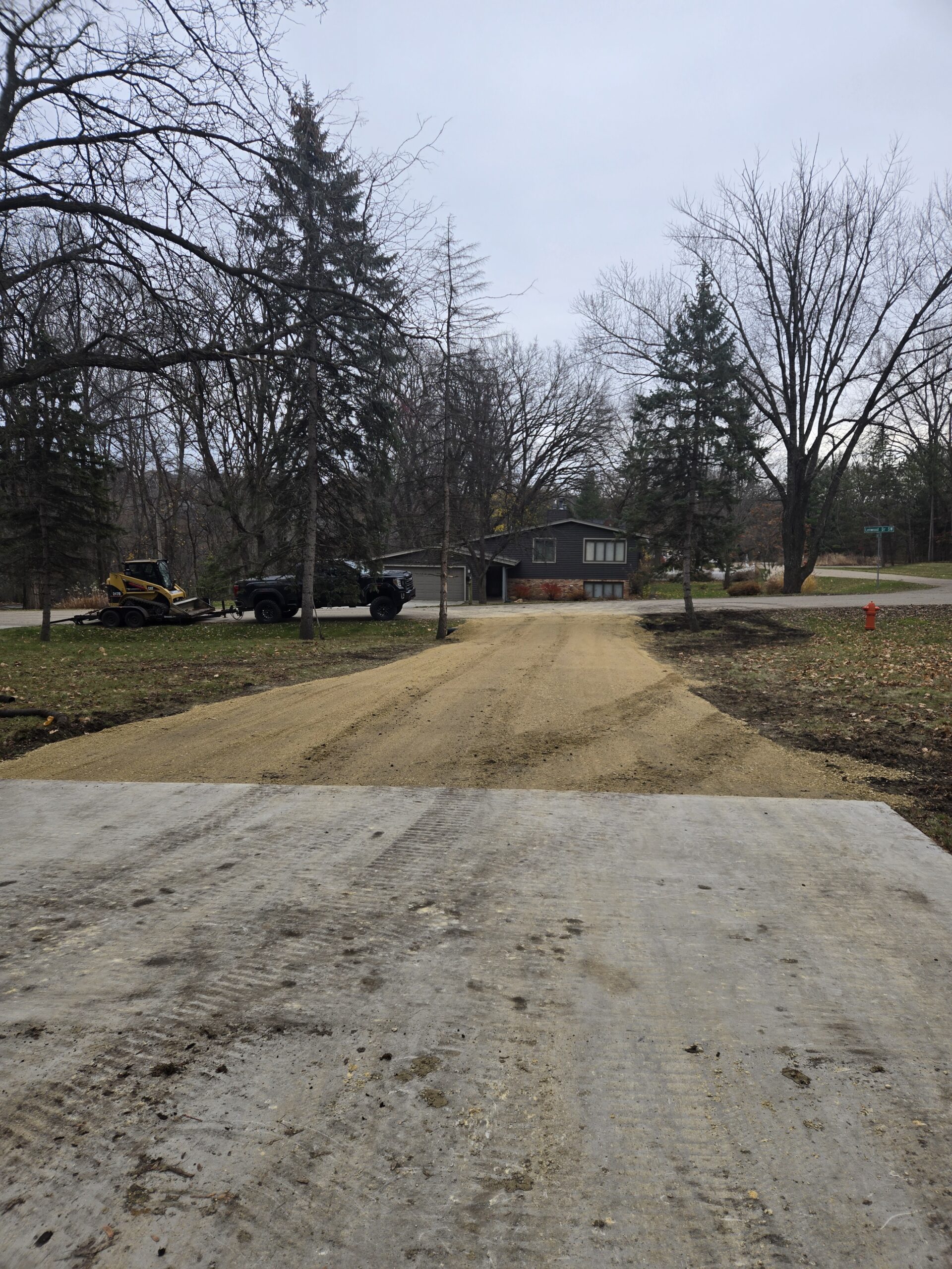 A muddy backyard with tire tracks leading to a house under construction.